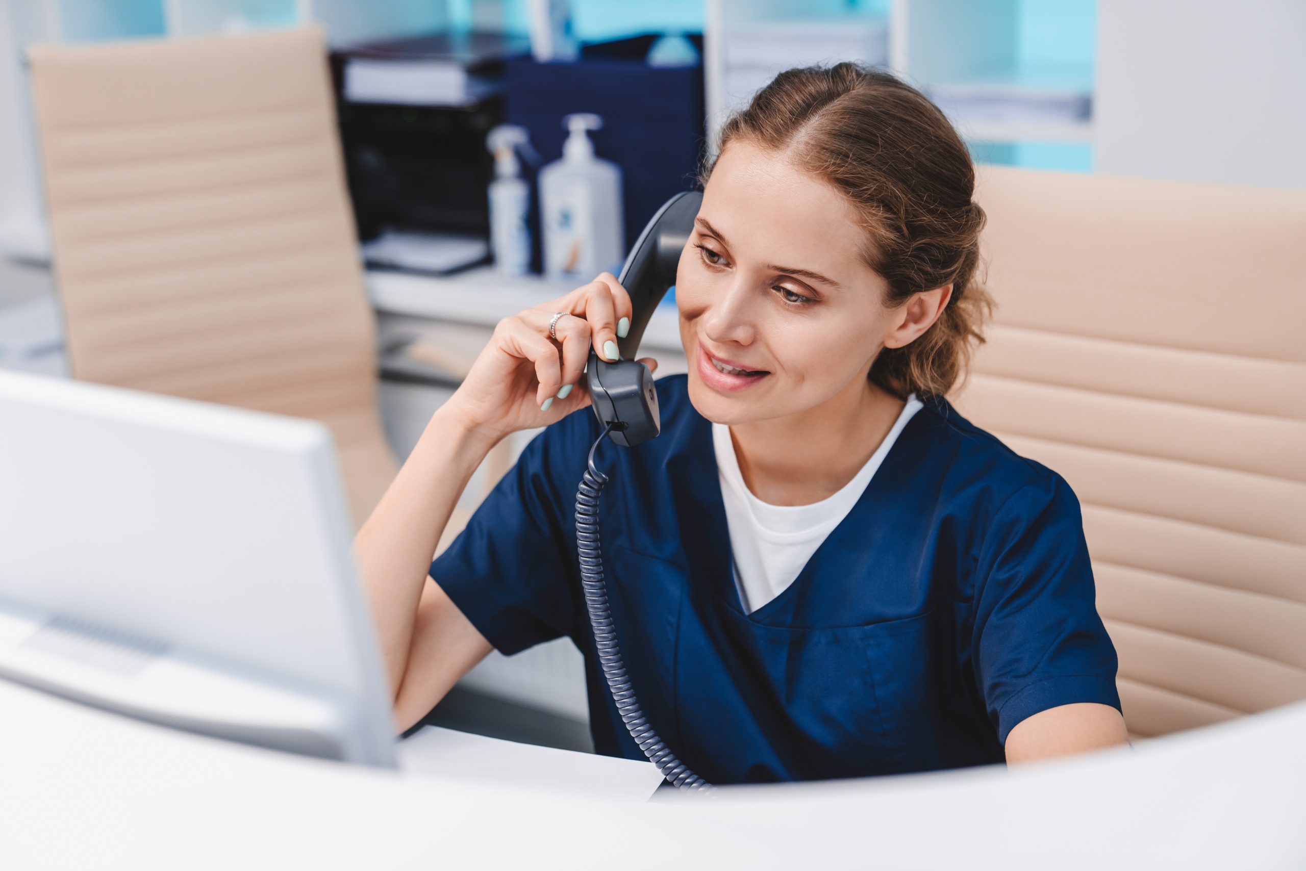 Woman on the phone with a computer in front of her at a desk.